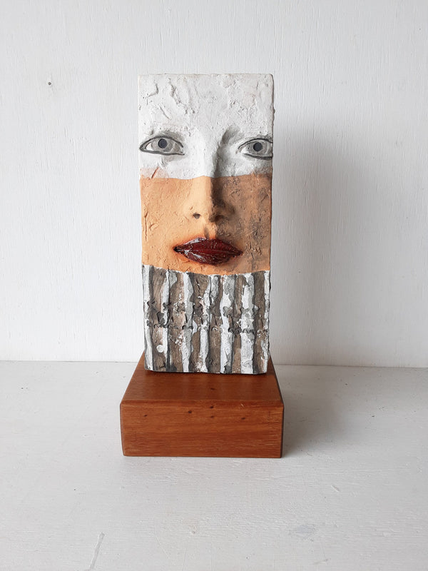 Modern sculpture head on timber plinth, ceramic female face in terracotta with black and white stripes