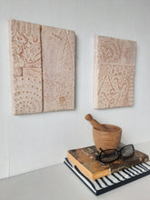 Pair of embossed ceramic wall plaques in pale terracotta and white, pastel textured sculptures