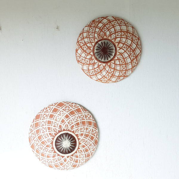 Pair of round white and terracotta ceramic wall plaques with geometric swirling pattern