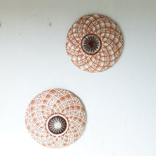 Pair of round white and terracotta ceramic wall plaques with geometric swirling pattern