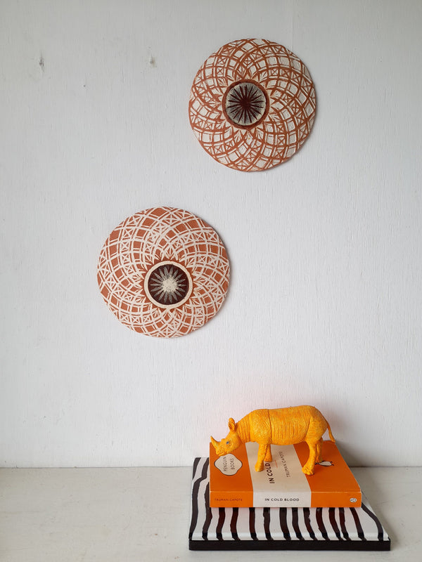 Pair of round white and terracotta ceramic wall plaques with geometric swirling pattern